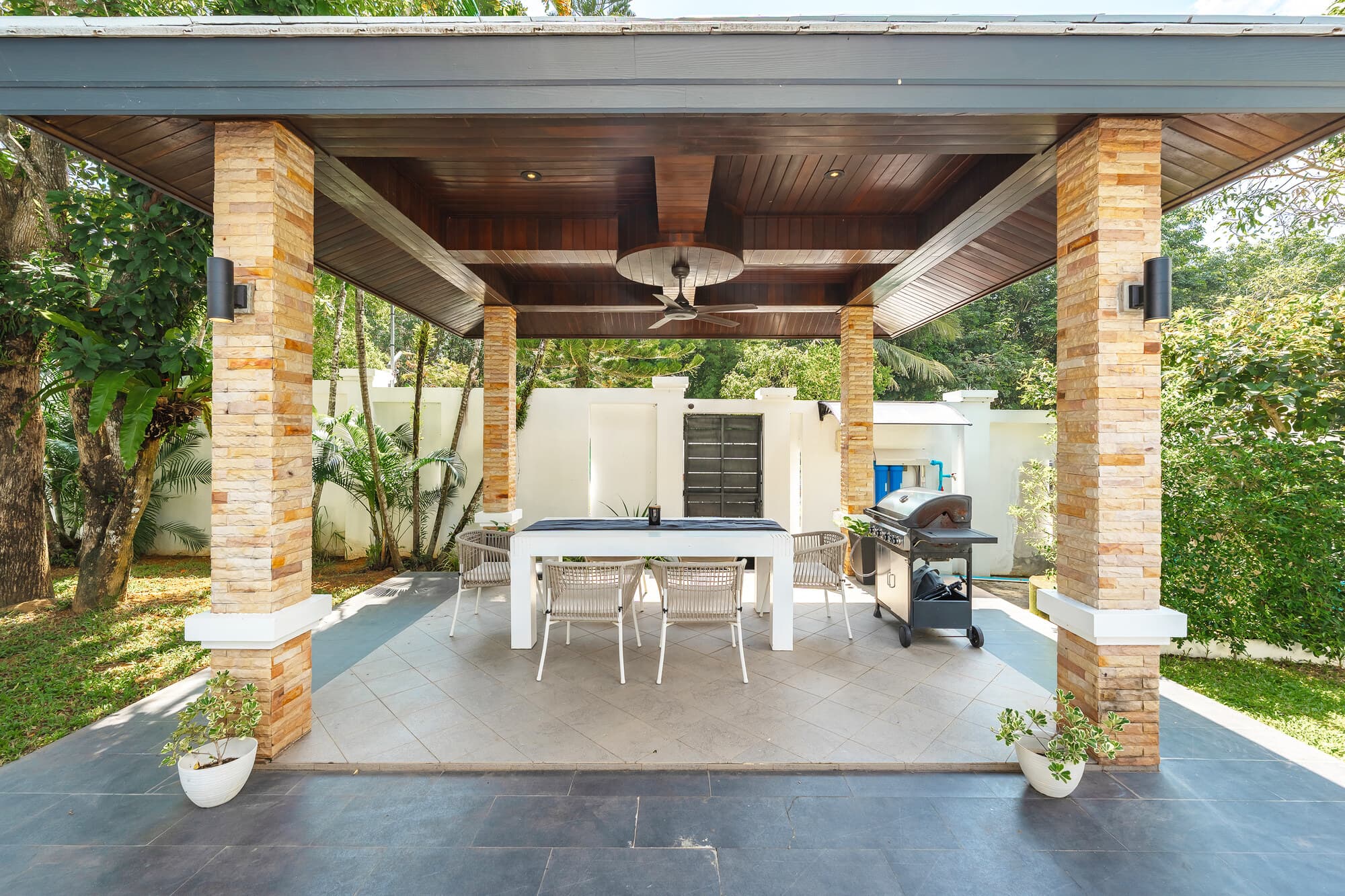 Covered outdoor cabana with dining table, barbecue, and garden outlook
