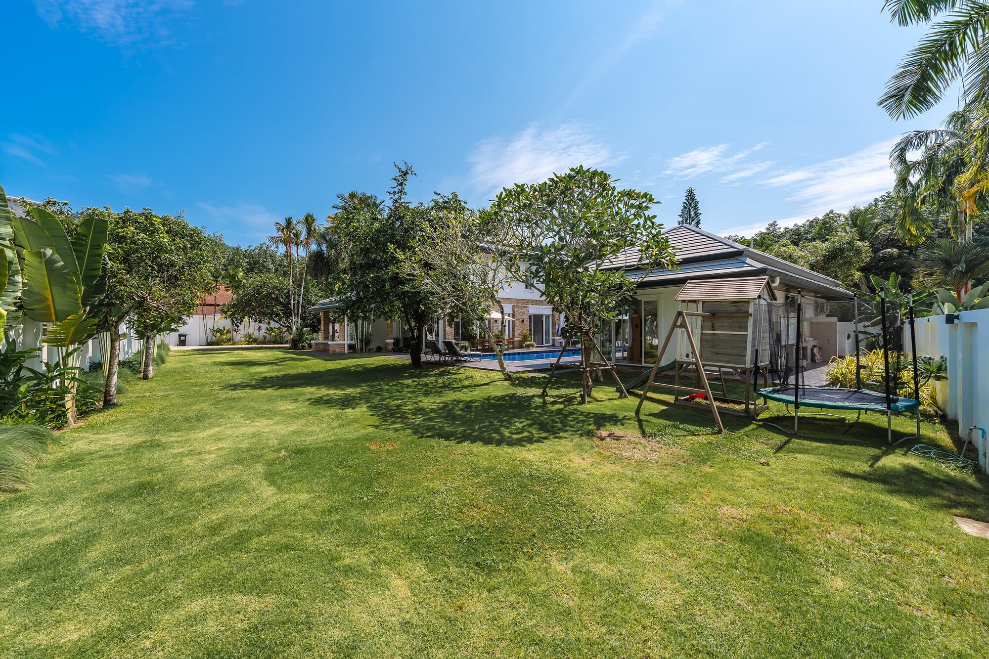 Large tropical lawn with mature trees and villa buildings beyond