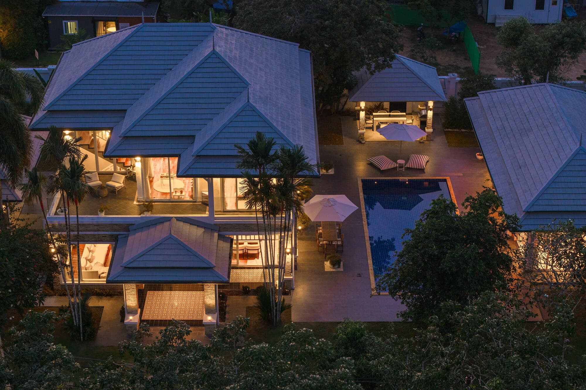 Aerial twilight view of the villa, illuminated pool, and cabana