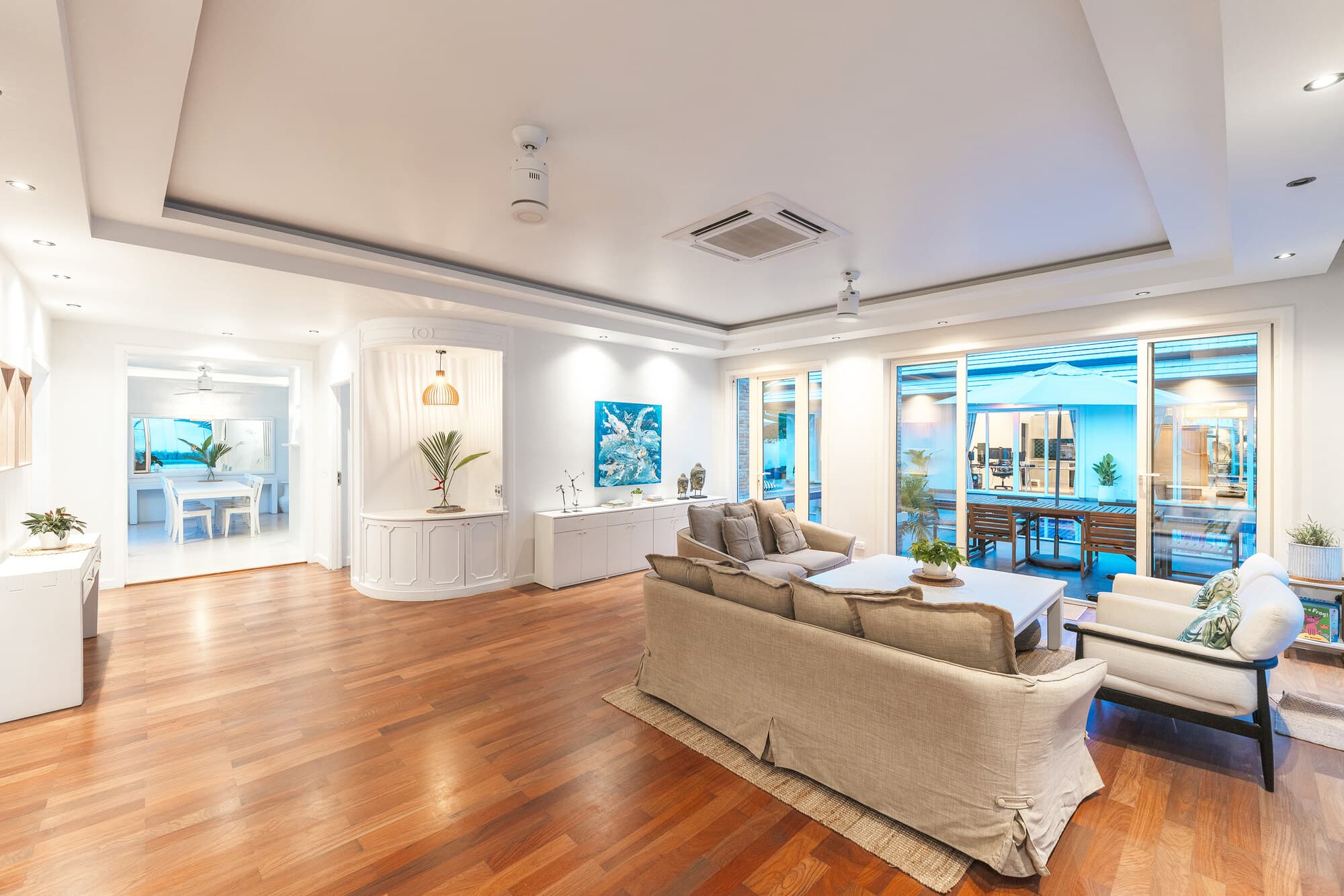 Evening living area with warm wood floors and view out to the pool terrace